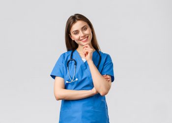 Mädchen in blauer Pflegeuniform mit Stethoskop, das nachdenklich lächelt, vor hellem Hintergrund.