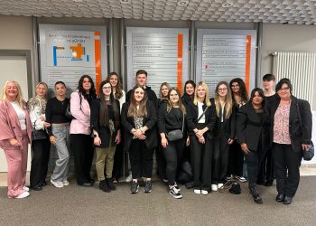 Eingespieltes Gruppenfoto vor einem Navigationsstand im Bildungszentrum Pirmasens, bestehend aus jungen Erwachsenen und zwei Lehrkräften, mit einer Notiztafel im Hintergrund.